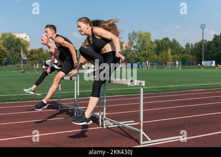 Zwei AthletInnen, Frau und Mann, die im Freien im Stadion Hürden laufen Stockfoto