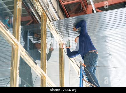 Baumeister Verwenden Sie einen elektrischen Schraubendreher, um die Blechdecke im Werk zu montieren. Stockfoto