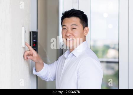Ein gutaussehender junger Geschäftsmann öffnet die Tür zum Büro durch eine moderne Türklingel. Geben Sie das Kennwort ein, und drücken Sie die Taste. Er sieht in die Kamera und lächelt. Stockfoto