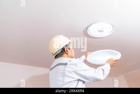 Nahaufnahme eines Elektrikers auf der Trittleiter installiert die Beleuchtung an der Decke im Büro. Stockfoto