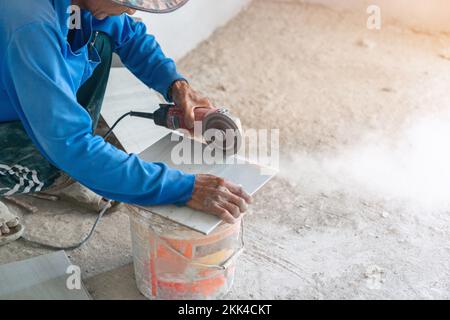 Bauarbeiter, der Bodenfliesen für Bauzwecke mit einem elektrischen Schleifen schneidet. Stockfoto