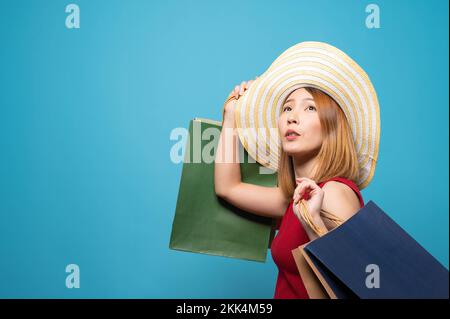 Ein Porträt einer jungen Thai-Frau mit Einkaufstaschen vor hellblauem Hintergrund Stockfoto