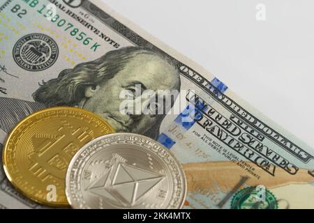 Physische Bitcoin- und Ethereum-Münzen über etwa 100-Dollar-Scheine. Kryptowährungsumtausch, Investitionskonzept. Stockfoto