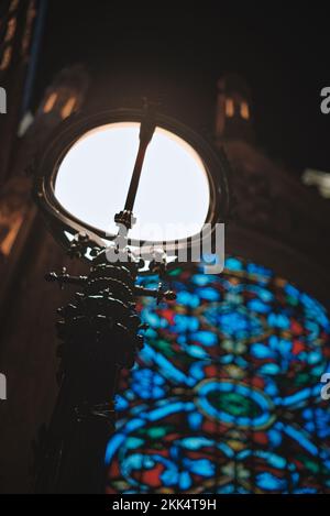 Eine vertikale Aufnahme einer beleuchteten Lampe an einem Buntglasfenster einer Kirche bei Nacht Stockfoto