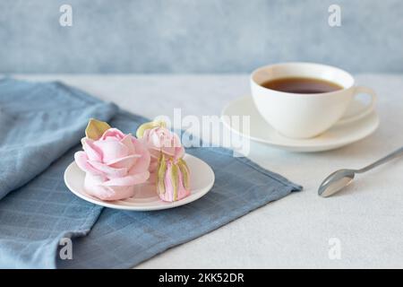 Teeset in einer Komposition mit marmelallow Blumen. Kaffeetasse auf einer Untertasse. Auf einem hellgrauen Hintergrund. Morgen belebende Tee-Party Stockfoto