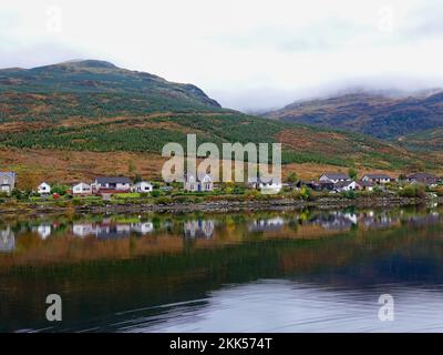 Morgennebel und Reflexionen in den Bergen, Häuser im Dorf Carrick Castle, Ufer von Loch Goil im Trossachs National Park, Schottland, Großbritannien. Stockfoto