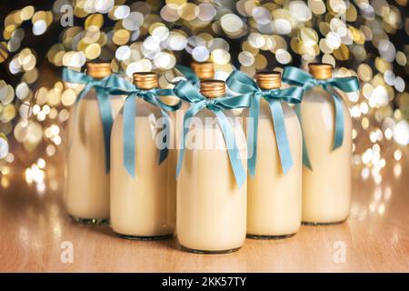 Hausgemachter Eierpunsch in Flaschen mit blauen Schleifen auf hellem, fleckigen Hintergrund Stockfoto