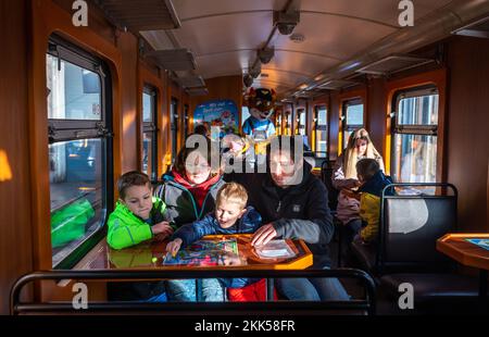 Oberwiesenthal, Deutschland. 25.. November 2022. Die Brüder Leon (6, l) und Jacob (4) spielen das Spiel „Dampf ab!“ Mit ihren Eltern Anja und Johannes frei während der Inbetriebnahme des neuen Sportwagens der Fichtelbergbahn. Es ist der erste Wildwaggon auf einer Schmalspurbahn in Sachsen. Die sächsische Dampfeisenbahngesellschaft (SDG) investierte 11.500 Euro in die Umrüstung und Konstruktion des Autos. Kredit: Kristin Schmidt/dpa/Alamy Live News Stockfoto