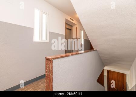 Landung eines Wohnwohnungsgebäudes mit einer Treppe mit rötlichen Terrazzoböden, Geländern mit rotem Marmor und einem grauen Metallaufzug Stockfoto