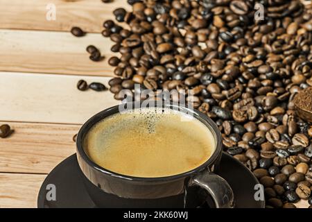 Ein frisch servierter Kaffee in einer Tasse neben einer Menge Bohnen, die zum Mahlen bereit sind Stockfoto