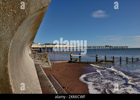 Der Pier und ein Teil der Ufermauer in Teignmouth, wo die gebogenen Rückläufe zu sehen sind, die die Wellen ablenken. Stockfoto