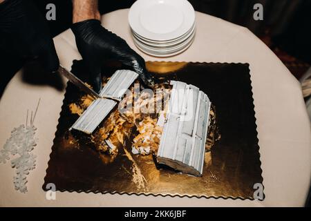 Fantastische Kuchen. Ein Koch mit schwarzen Handschuhen schneidet eine Schokoladenkuchen-Hochzeitstorte auf. Der Hochzeitskuchen ist innen köstlich auf schwarzem Hintergrund. Großer Kuchen in Weiß Stockfoto