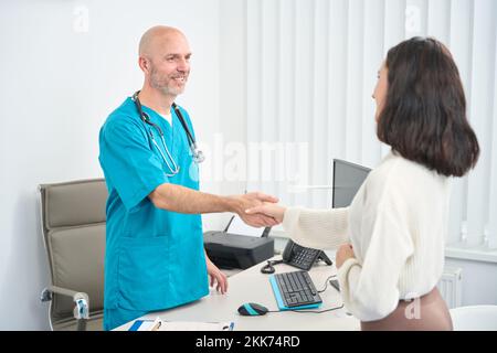 Der Patient schüttelt sich die Hände mit dem Arzt, während er sich im Arbeitsbereich befindet Stockfoto