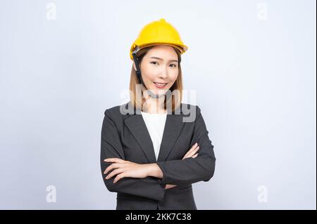 Ein Porträt einer jungen asiatischen Geschäftsfrau, die einen gelben Sicherheitshelm im formellen Anzug auf weißem Hintergrund trägt Stockfoto