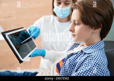 Zahnarztfrau zeigt dem jungen Patienten ein Zahnbild auf dem Klemmbrett Stockfoto