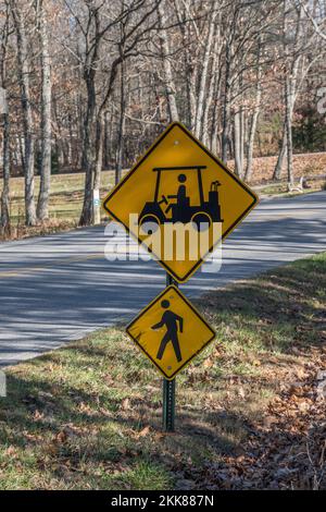 Zwei Schilder auf einem Stab entlang der Straße neben einem Golfplatz und Pfaden zeigen einen Golfwagen und Fußgängerüberquerung vor uns, um sich vorsichtig zu nähern Stockfoto