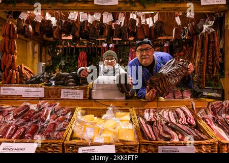 Breitnau, Deutschland. 25.. November 2022. Sandra Kästner und Stefan Gutscher stehen am Weihnachtsmarkt in Ravennaschlucht an ihrem Stand und halten Schwarzwurst und Schwarzwaldspeck in den Händen. Nachdem der Weihnachtsmarkt in der Ravennaschlucht aufgrund der Corona-Pandemie im Jahr 2020 eingestellt werden musste und im folgenden Winter 2021 nur für einige Tage geöffnet werden konnte, Dieses Jahr dürfen Besucher an allen vier Adventswochenenden den Weihnachtsmarkt unter dem Viadukt der Höllentalbahn besuchen. Kredit: Philipp von Ditfurth/dpa/Alamy Live News Stockfoto