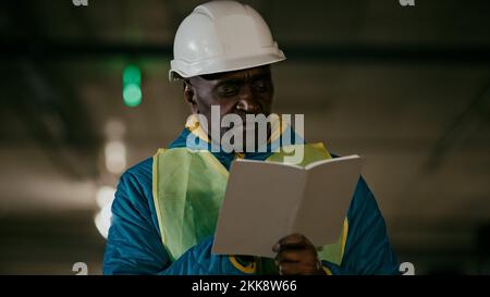 Erfahrener Arbeiter Ingenieur mit Schutzhelm inspiziert Raum schreibt Daten in Notizbuch konzentrierter erfahrener Vorarbeiter erstellt Stockfoto