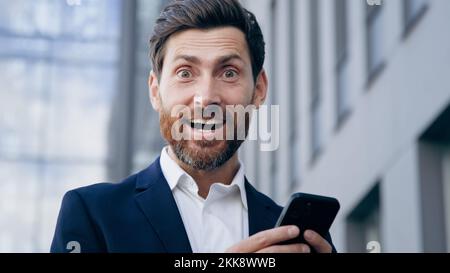 Aus nächster Nähe aufgeregter überraschter Mann, der E-Mail-Benachrichtigungen auf dem Mobiltelefon liest und gute Nachrichten erhält Happy zufriedener emotionaler Geschäftsmann gewinnt online Stockfoto