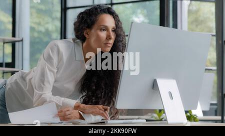 Junge attraktive hispanische Frau, professionelle Managerin, Entwickler, die in modernen Büros arbeitet, fokussierte Geschäftsfrau, die elektronische Informationen überprüft Stockfoto