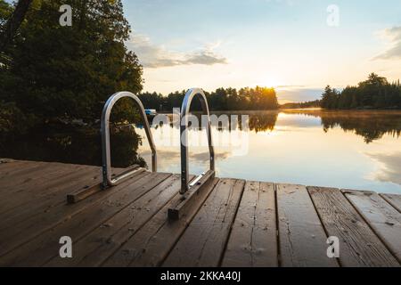 Die Sonne geht über einem Dock an einem ruhigen See auf Stockfoto
