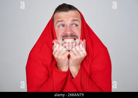 Ein Mann zieht Kleider auf den Kopf, versucht sich in tiefer Erstaunung und Angst zu verstecken. Stockfoto