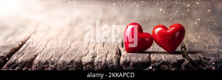 Zwei Herzen aus rotem Marmorglas auf einem rustikalen Holztisch mit Sonnenlicht und Bokeh - Valentinstag Stockfoto