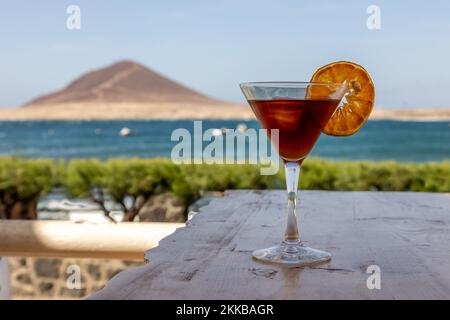 Ein Blut- und Sandcocktail, ein Mixgetränk in einem Glas, dekoriert mit einem Zitronenscheibe und Blick auf den Strand Stockfoto