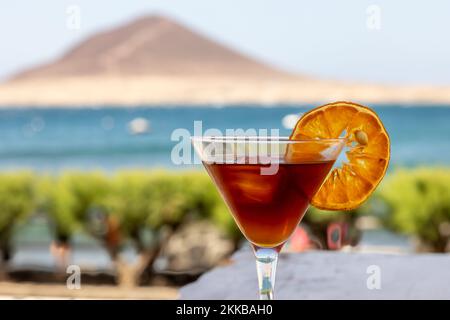 Eine Nahaufnahme eines Blut- und Sandcocktails, Mixgetränk in einem Glas, dekoriert mit einem Zitronenscheibe am Strand Stockfoto