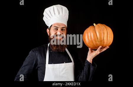 Bärtiger Koch in Koch-Uniform und Schürze mit Kürbis. Gesundes Bio-Gemüse. Herbstessen Stockfoto