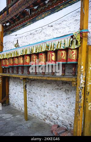 Mehrere identische, bemalte Gebetsräder säumen die Mauer entlang einer engen Straße in Thimphu, Bhutan. Die Räder sind landesweit weit weit verbreitet. Stockfoto