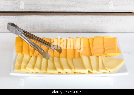 Eine Nahaufnahme zweier Arten von Käsescheiben auf einem weißen Teller in einem Buffet Stockfoto