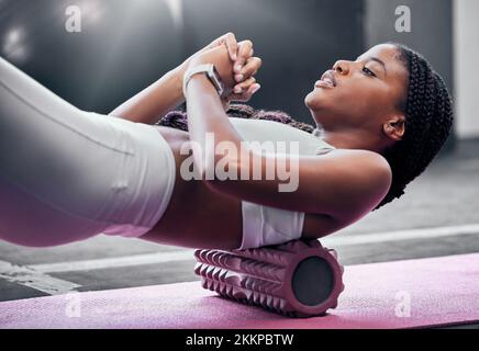 Fitness, Training und Schaumstoffwalze mit einer schwarzen Frau im Fitnessstudio, Training während eines Trainings für Gesundheit. Yoga, Wellness und Pilates mit einer Sportlerin Stockfoto