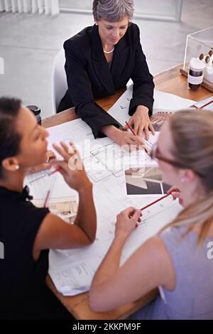 Es geht um die Details. Eine Gruppe weiblicher Architekten, die gemeinsam an einem Projekt an einem Konferenztisch arbeiten. Stockfoto