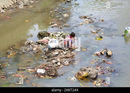 Ein Mann gräbt durch den Müll, der auf dem Fluss schwimmt, auf der Suche nach etwas von Wert. Bali, Indonesien - 03.01.2018 Stockfoto