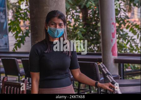 Eine kambodschanische Kellnerin, die während der COVID-Pandemie eine Gesichtsmaske trägt, in einem Open-Air-Restaurant am Flussufer. Phnom Penh, Kambodscha. © Kraig Stockfoto