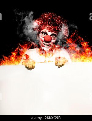 Unheimlich Porträt EINES gruseligen Zirkus Clown hält EINEN Blank Copyspace-Board, während in Flammen des Feuers in EINEM stehen Hot Halloween Specials Konzept Stockfoto