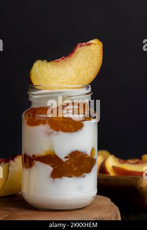 Joghurt aus frischer Milch mit süßer Pfirsichmarmelade und frischen Pfirsichen, köstlicher Joghurt mit Pfirsichgeschmack Stockfoto