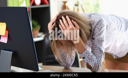 Stressige Frau beugt sich über den Tisch und hält den Kopf mit den Händen im Büro Stockfoto