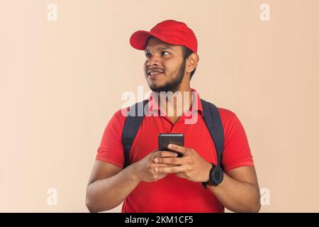Selbstbewusster junger Zusteller, der mit dem Handy wegsieht Stockfoto