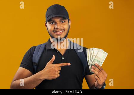 Junger Liefermann mit lächelnden indischen Rupien-Banknoten Happy Pointing mit Hand und Finger Stockfoto