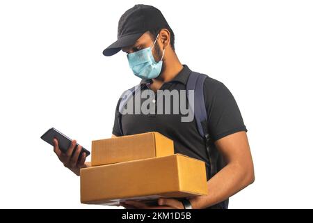 Portrait von Young Delivery man trägt Gesichtsmaske Holding Paket mit Handy Stockfoto