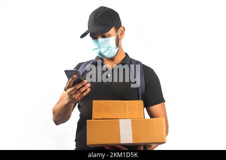 Glücklicher indischer Liefermann mit Smartphone und Paketkiste in schwarzer Uniform Stockfoto