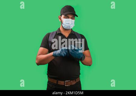 Portrait von Young Delivery man trägt Gesichtsmaske und Handschuh mit Handy Stockfoto