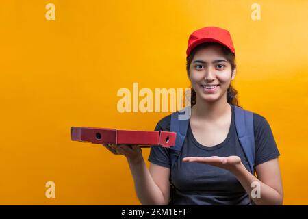 Fröhliche junge Lieferfrau, die eine Pizzaschachtel hält und zeigt Stockfoto