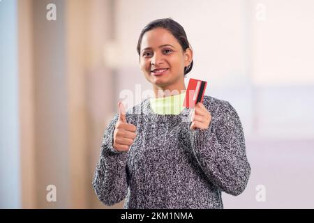 Porträt einer glücklichen jungen Frau mit Kreditkarte und Daumen hoch Stockfoto