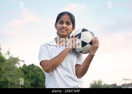 Ein junges Mädchen, das auf dem Feld steht und den Fußball hält Stockfoto