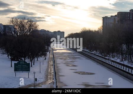 Die Sonne geht an einem teilweise bewölkten Morgen in Ottawa auf und sieht am verschneiten späten Herbsttag über einen gefrorenen Rideau Canal. Stockfoto