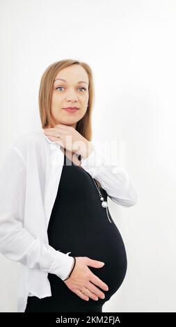 Porträt einer jungen schwangeren Frau auf weißem Hintergrund. Er hält seine Hände auf seinem aufgeblähten Magen. Liebeskonzept Stockfoto