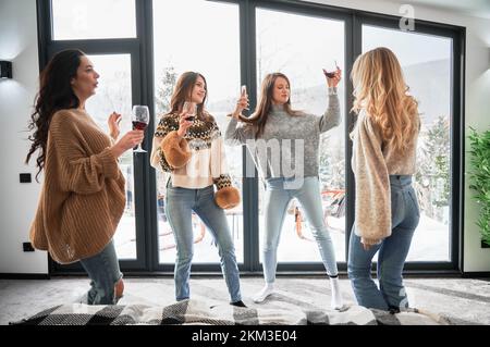 Junge Frauen genießen Winterwochenenden im modernen Scheunenhaus. Vier Mädchen, die Spaß haben und Rotwein trinken. Stockfoto